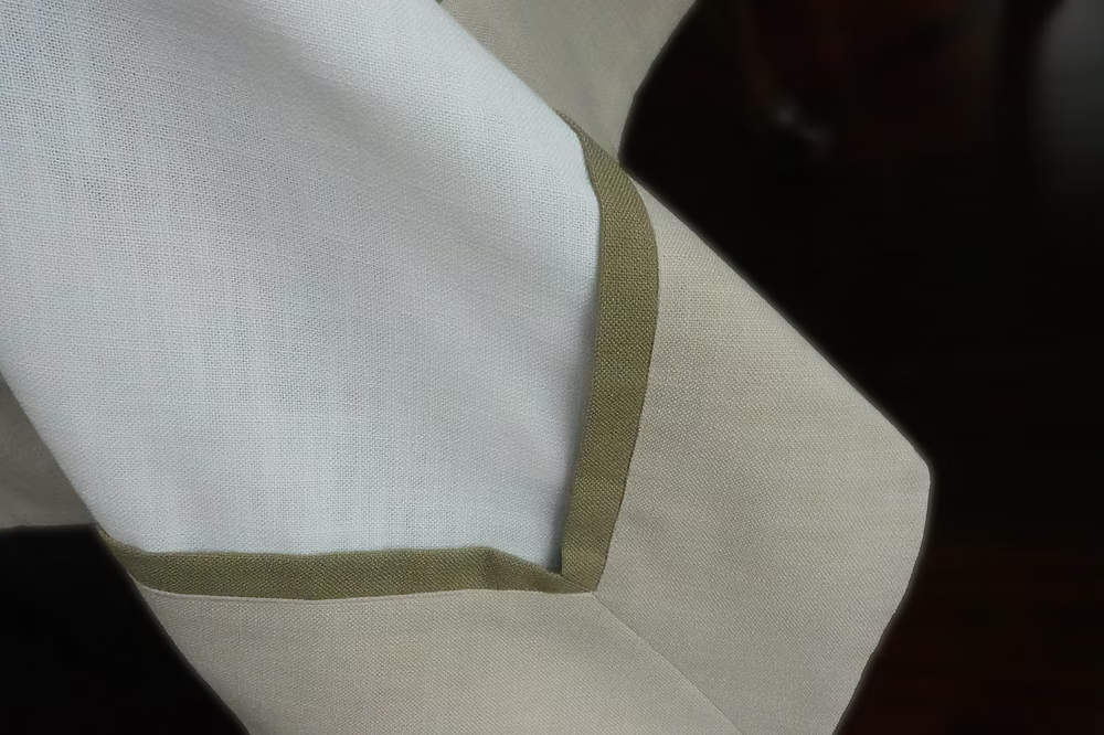 22 Maggio Istanbul Cavalcanti Designer Table Cloth-Close-up of a white fabric with green trim on a dark background