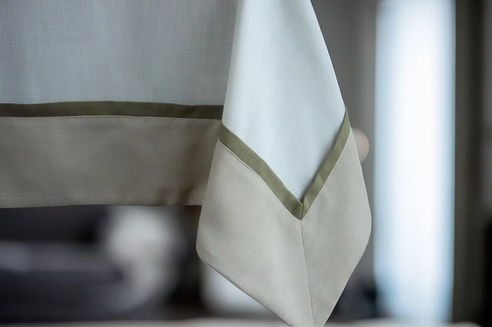 22 Maggio Istanbul Cavalcanti Designer Table Cloth-Close-up of a beige and white fabric with green trim against a blurred background