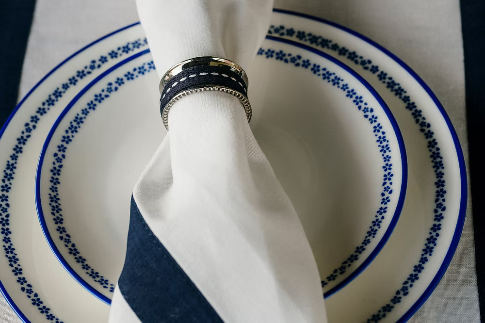 22 Maggio Istanbul Marinaio Linen Napkin Set of 4-White napkin with a blue stripe and decorative ring on a blue and white patterned plate.