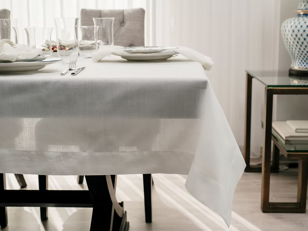 22 Maggio Istanbul Sereno Linen Tablecloth-Dining table set with white tablecloth, plates, and cutlery in a bright room.