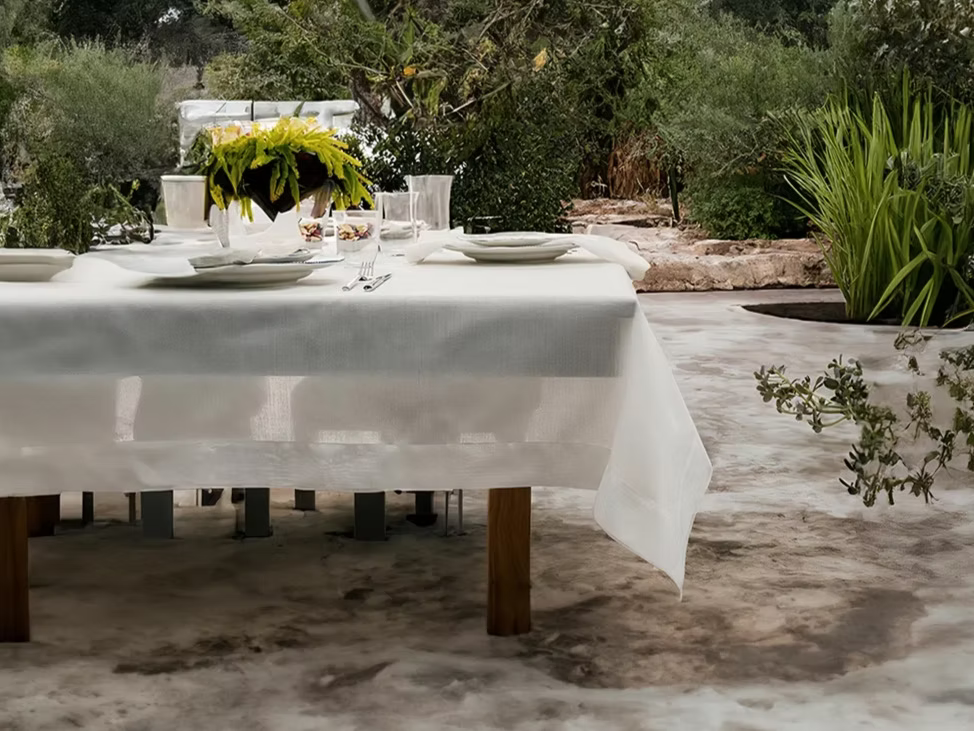 22 Maggio Istanbul Sereno Linen Tablecloth-Dining table set with white tablecloth, plates, and glasses outdoors.