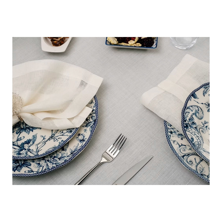 22 Maggio Istanbul Sereno Linen Tablecloth-Dining table setting with blue and white patterned plates, silverware, and white napkins on a gray tablecloth.