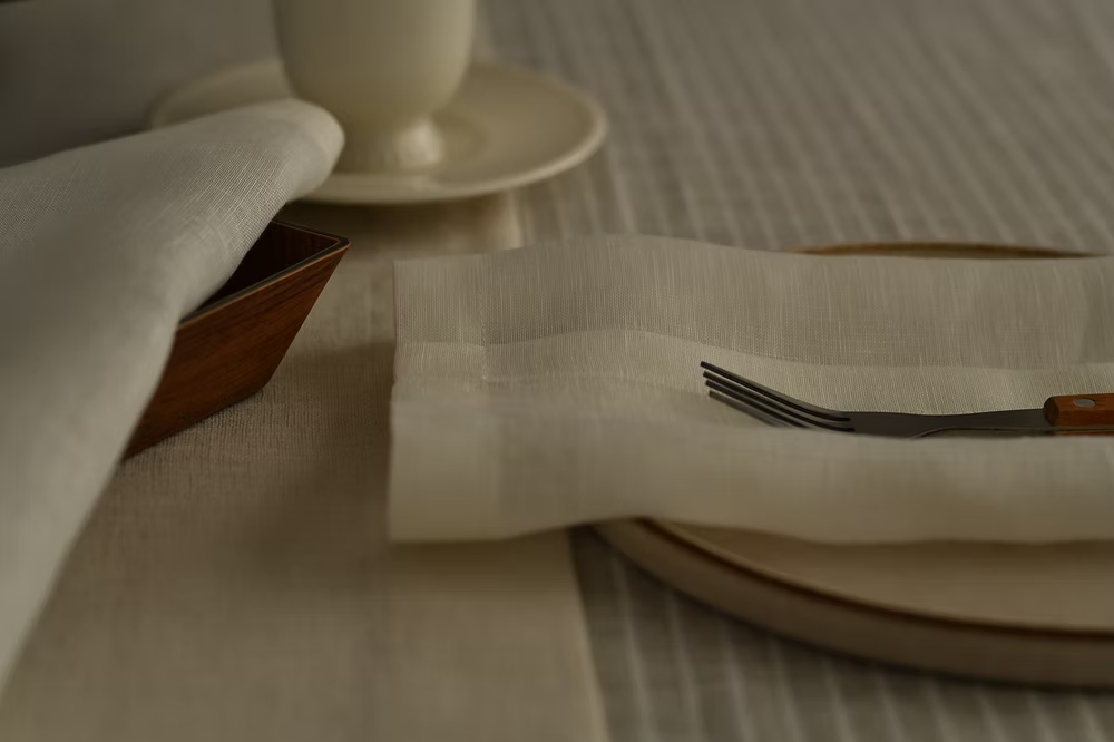 22 Maggio Istanbul Terreno Beige Linen Napkin Set of 4-Dining table setting with plates, fork, and cup on a textured surface