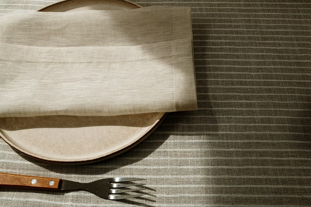 22 Maggio Istanbul Terreno Beige Linen Napkin Set of 4-Plated dish with a folded beige napkin on a textured tablecloth, accompanied by a fork.