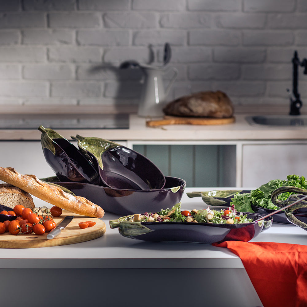 Bordallo Pinheiro Aubergine Salad Bowl-Kitchen counter with bowls of salad, eggplants, and bread, with a blurred kitchen background.