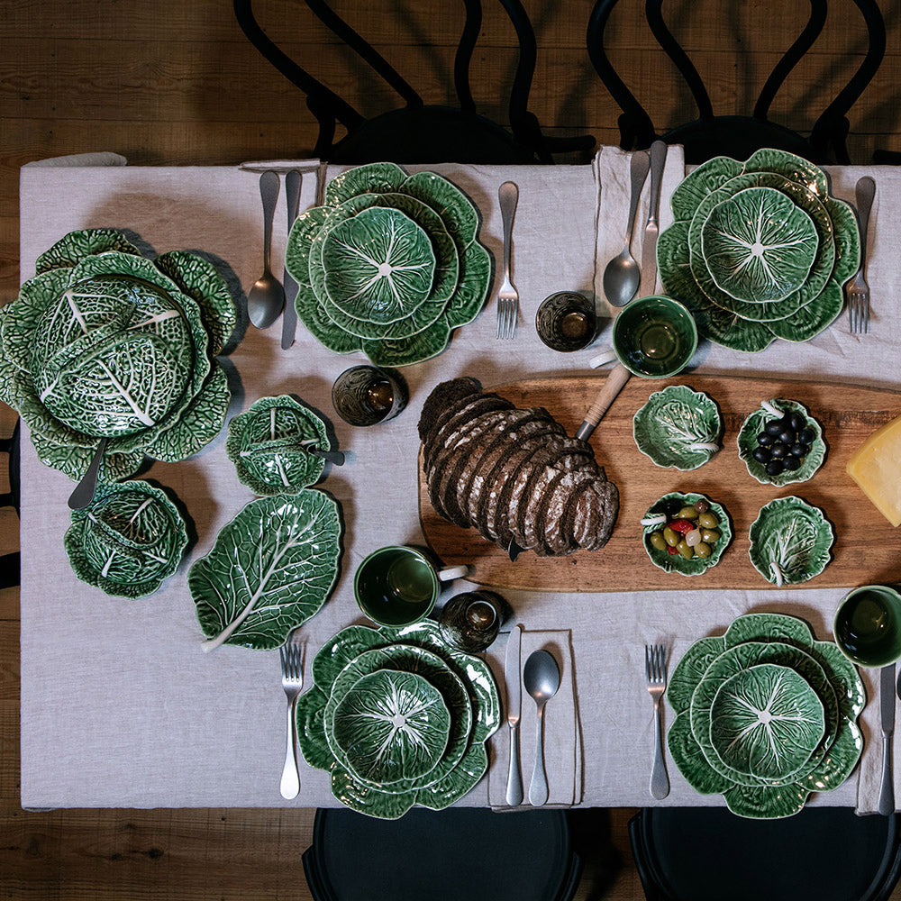 Bordallo Pinheiro Cabbage Chip & Dip Bowl-Dining table set with green leaf-patterned plates and a cutting board with bread and small dishes.