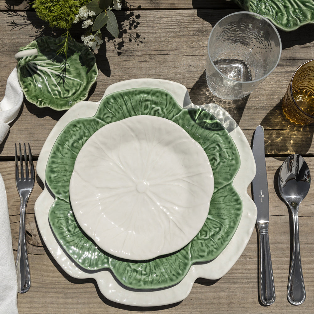 Bordallo Pinheiro Cabbage Dinner Plate-Green and white ceramic plate on a wooden table with cutlery and glasses.