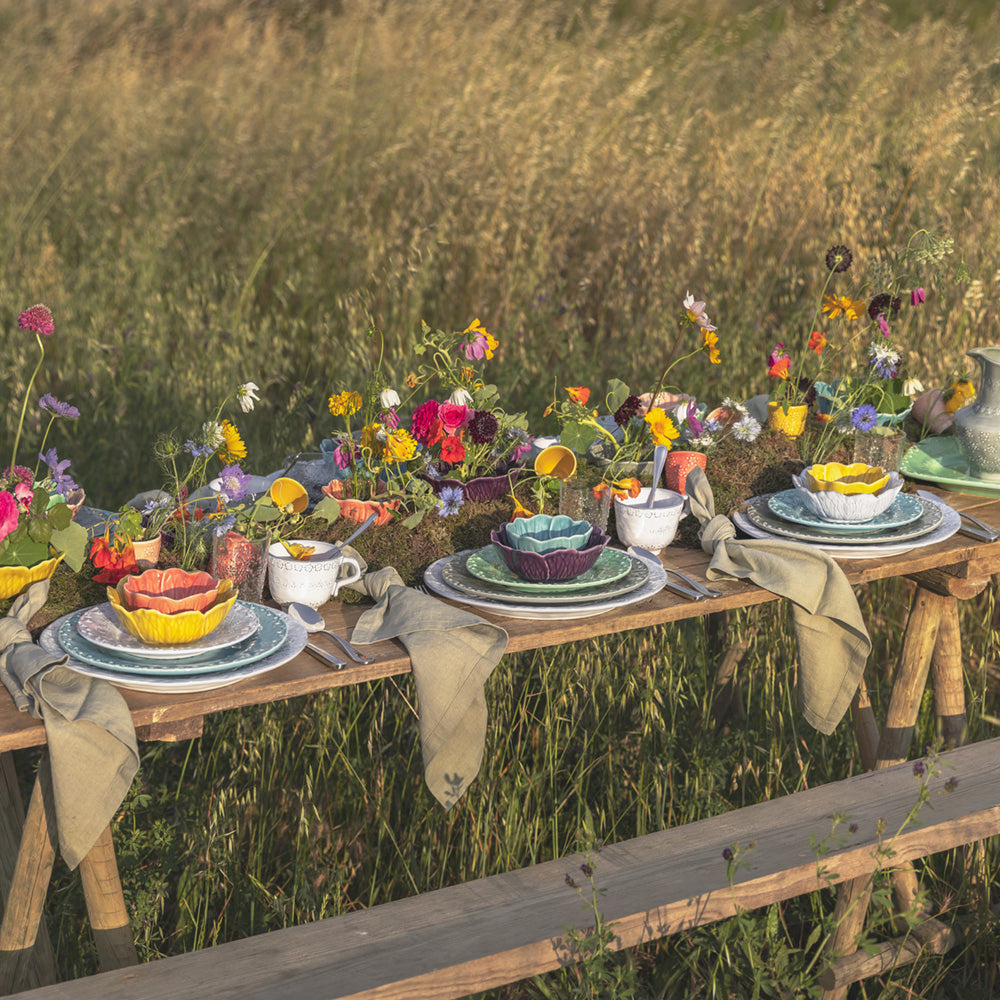 Bordallo Pinheiro Flora Dessert Plate-Dining table set with plates, cups, and flowers in a natural outdoor setting
