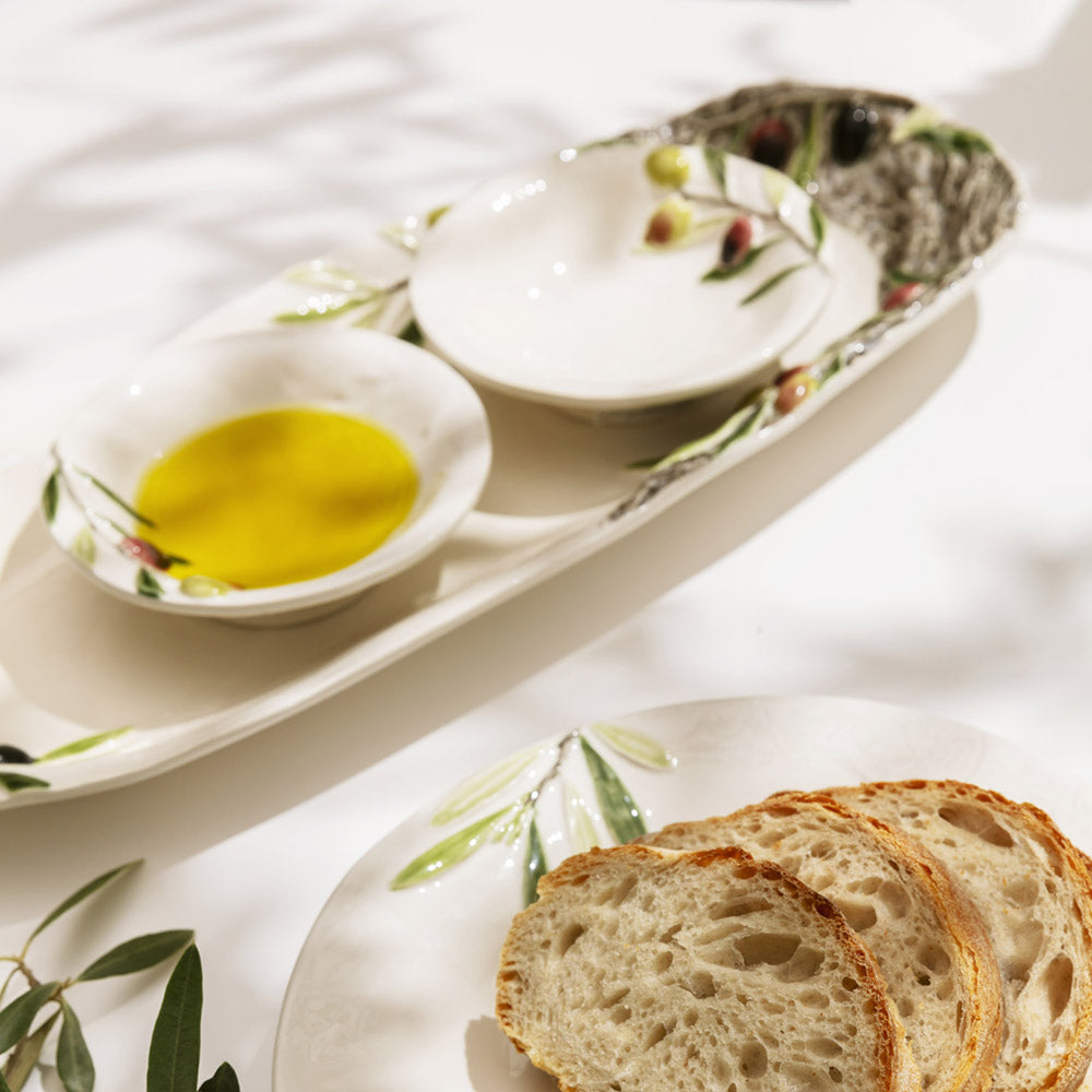 Bordallo Pinheiro Olival Platter-Bread slices on a decorative plate with olive oil in a bowl on a white surface.