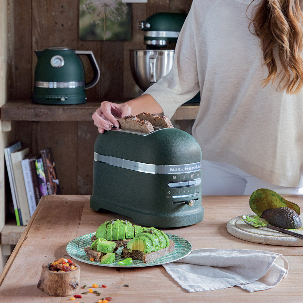 Person using a green KitchenAid Bread toaster in a kitchen setting with food on the counter.
