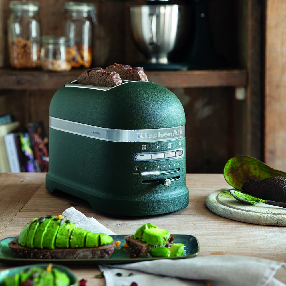 Green KitchenAid Bread toasteron a wooden table with avocado toast and ingredients.
