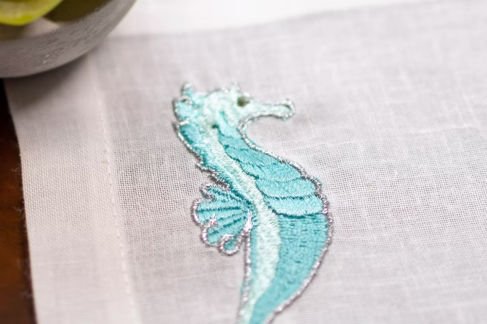 Cavallo Linen Coasters Set of 4-Embroidered blue seahorse design on light fabric