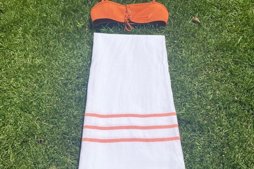 Coral Beach Towel-Orange bikini top and white towel with orange stripes on grass