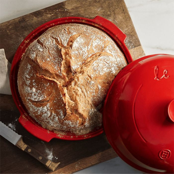 Emile Henry Bread Baker-Loaf of bread in a red ceramic dish on a wooden surface