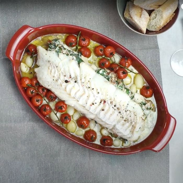 Emile Henry Covered Fish Steamer-Baked fish dish with cherry tomatoes and garlic in a red oval baking dish on a gray surface.