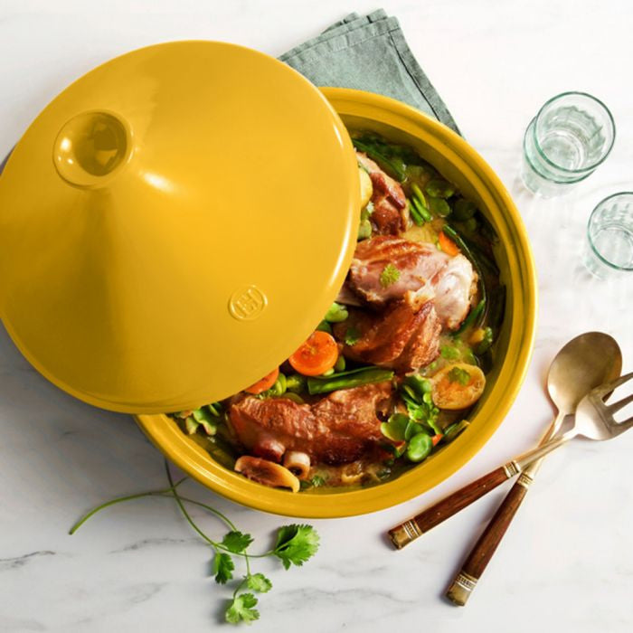 Emile Henry Flame Tagine-Yellow casserole dish with a lid, containing meat and vegetables on a marble surface.