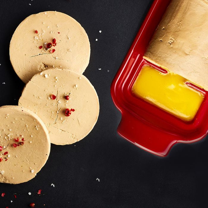 Emile Henry Foie Gras Medallion Terrine-Three round beige food items with red specks on a black surface, next to a red container with yellow butter.