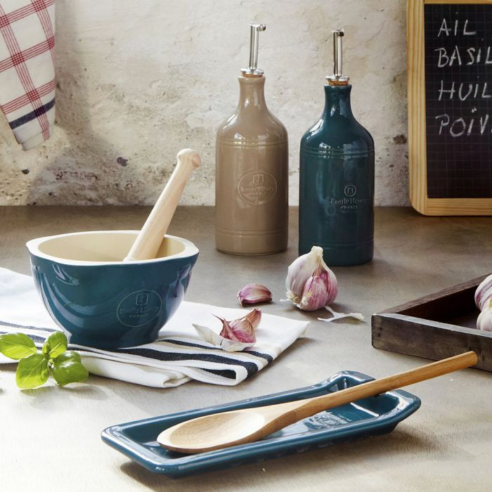 Emile Henry Oil Cruet-Kitchen counter with blue ceramic bowl, wooden spoon, and olive oil bottles.