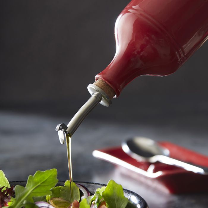 Emile Henry Oil Cruet-Red bottle pouring olive oil onto a salad with a dark background