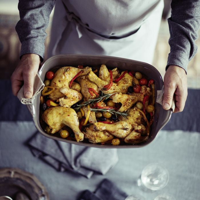 Emile Henry Rectangular Oven Dish-Person holding a dish of roasted chicken with vegetables on a table.