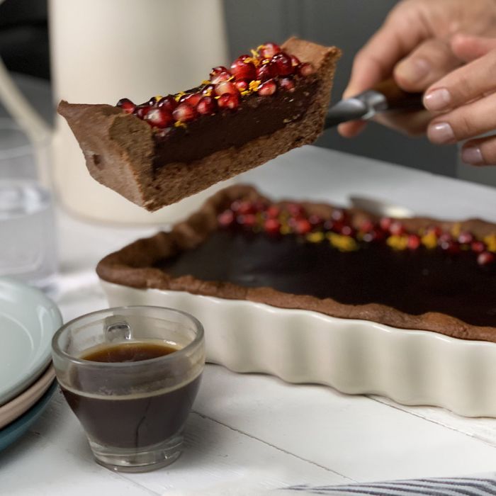 Emile Henry Slim Rectangular Tart Dish-Chocolate tart with pomegranate seeds being served with a cup of coffee on a white surface.