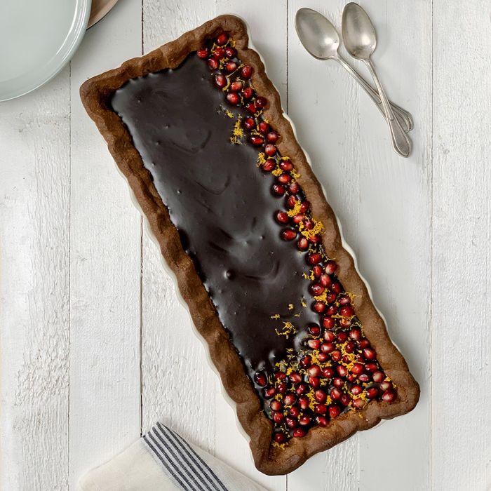 Emile Henry Slim Rectangular Tart Dish-Long rectangular chocolate dessert with pomegranate seeds on a white wooden surface.