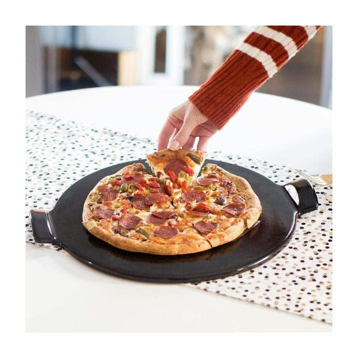 Emile Henry Smooth Pizza Stone, 36cm-Person taking a slice of pizza from a black pizza stone on a white table.