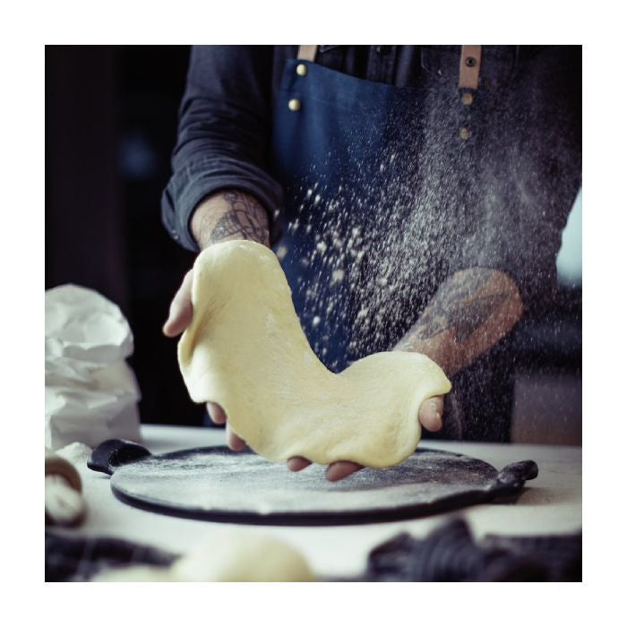 Emile Henry Smooth Pizza Stone, 36cm-Person kneading dough with flour in the air, wearing a dark apron.