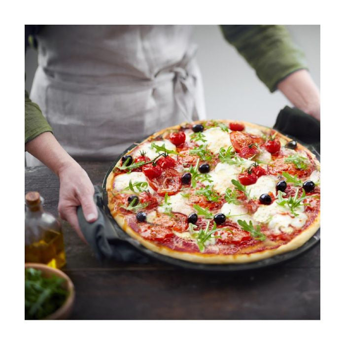 Emile Henry Smooth Pizza Stone, 36cm-Person holding a pizza with various toppings on a wooden table