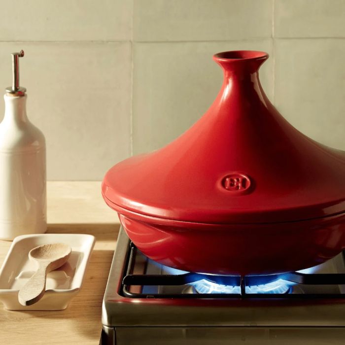 Emile Henry Tagine, 26cm-Red ceramic tagine on a gas stove with a kitchen setting in the background.