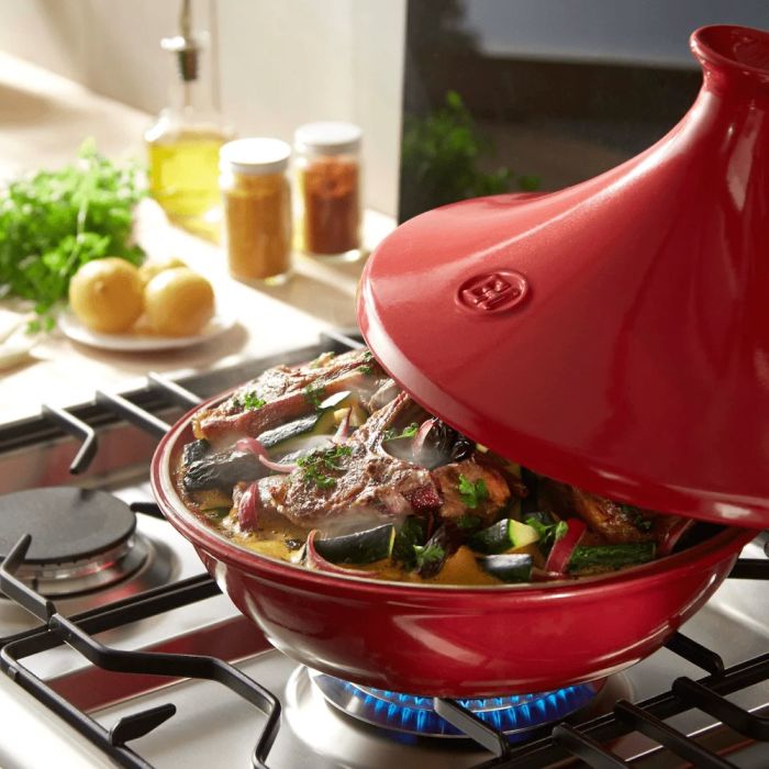 Emile Henry Tagine, 26cm-Red tagine with food on a stove top, surrounded by kitchen items.