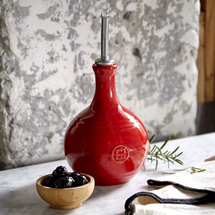 Emile Henry Vinegar Cruet-Red ceramic oil dispenser on a marble surface with a bowl of olives and rosemary.