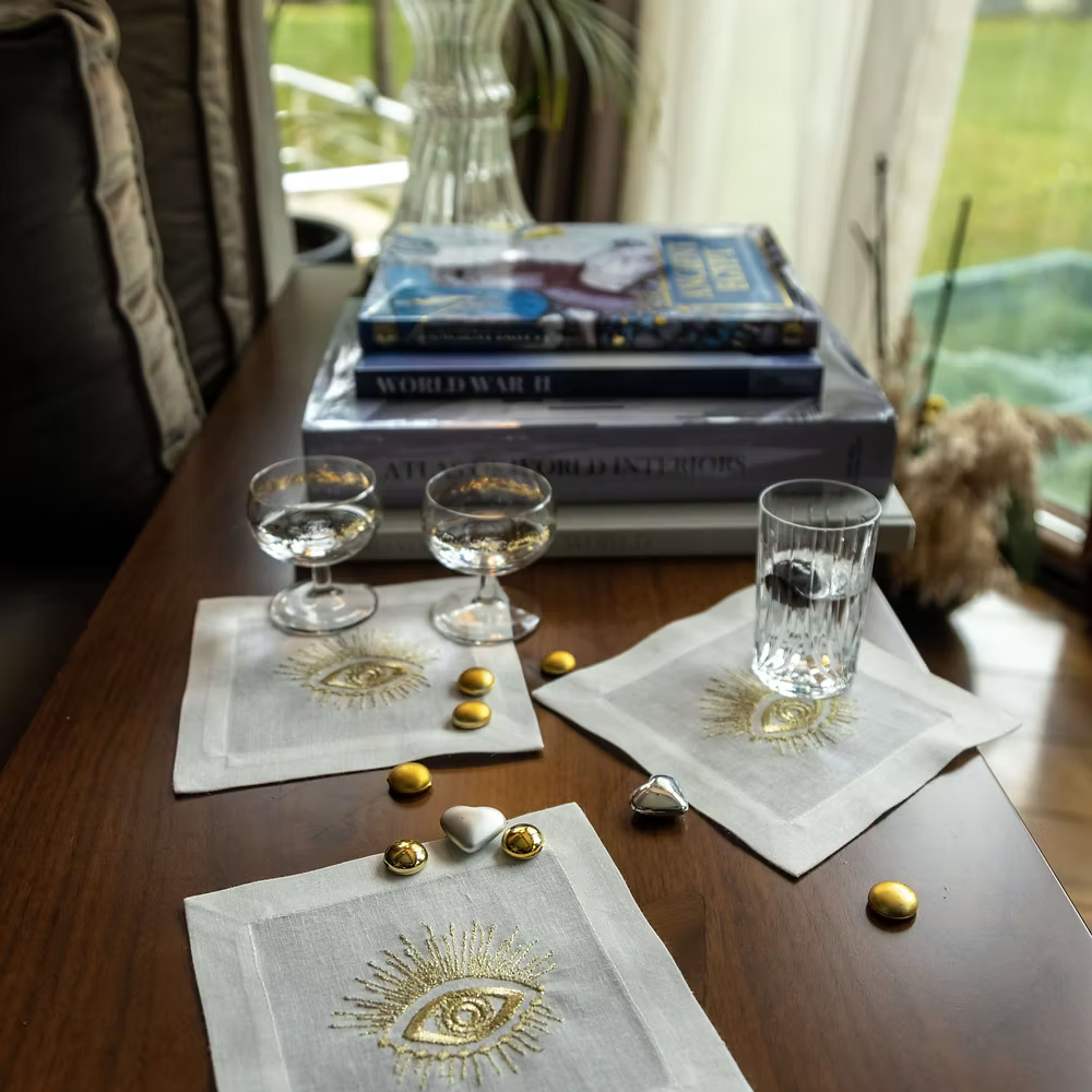 Fatima Linen Coasters Set of 4-Decorative table setting with books, glasses, and embroidered napkins on a wooden surface.