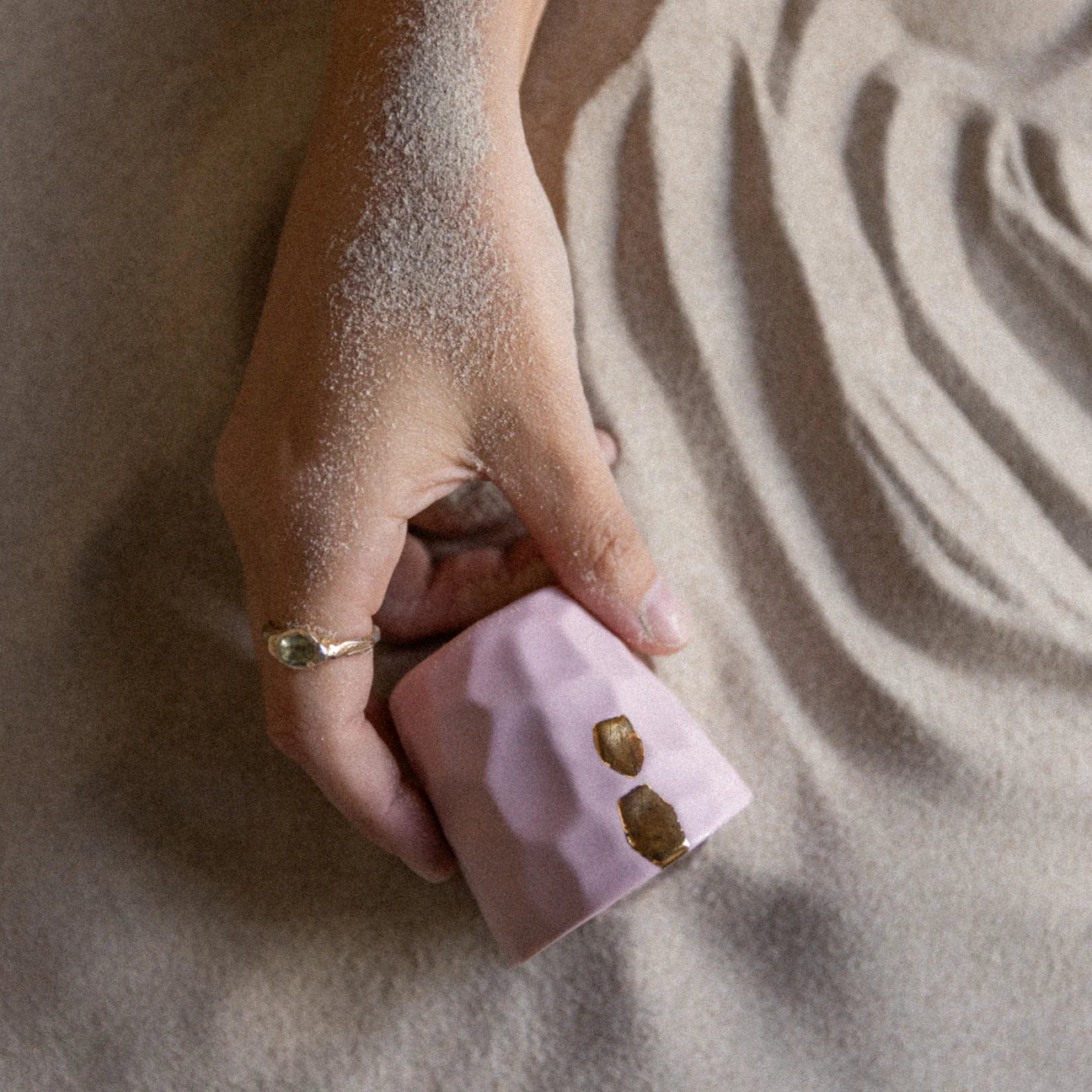 Hand holding a pink Gahwa cups with gold accents on sand