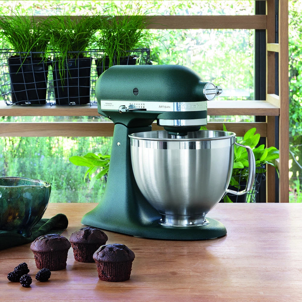 KitchenAid Green stand mixer on a wooden table with muffins and blackberries, plants in the background