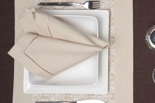Latte Dinner Napkin Set of 4-Plated dinner setting with folded napkin, fork, and knife on a textured surface.