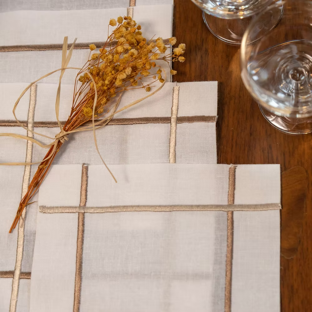 Linee Linen Coasters Set of 4-Placemat with grid pattern on a wooden table with dried flowers and glasses.