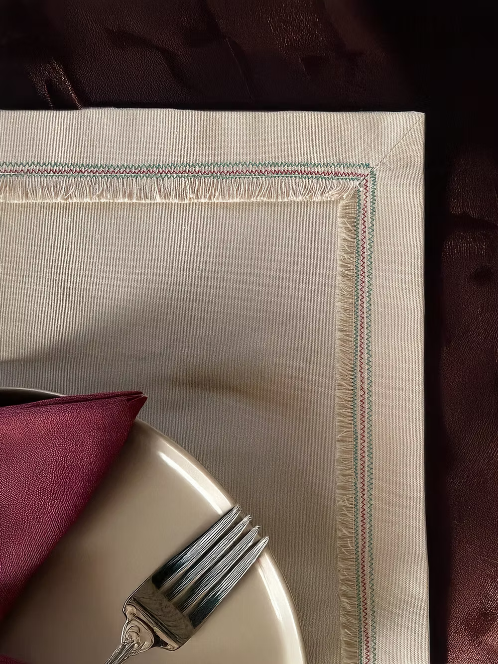 Nappina Placemat Set of 4-Beige placemat with a red napkin and silver fork on a dark surface