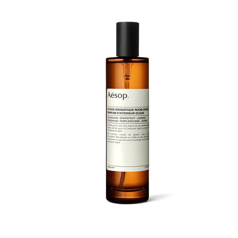 A brown bottle of Aesop Olous Aromatique Room Spray with a white label, standing upright against a black background.