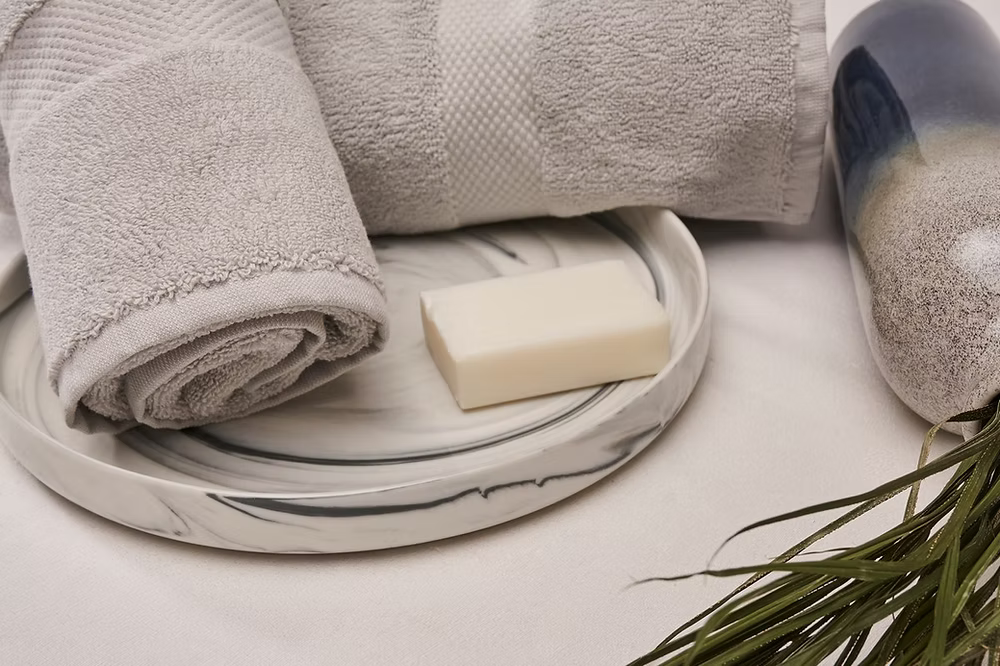 Roma Towel Set-Gray towel on a marble tray with a bar of soap and a plant on a light background