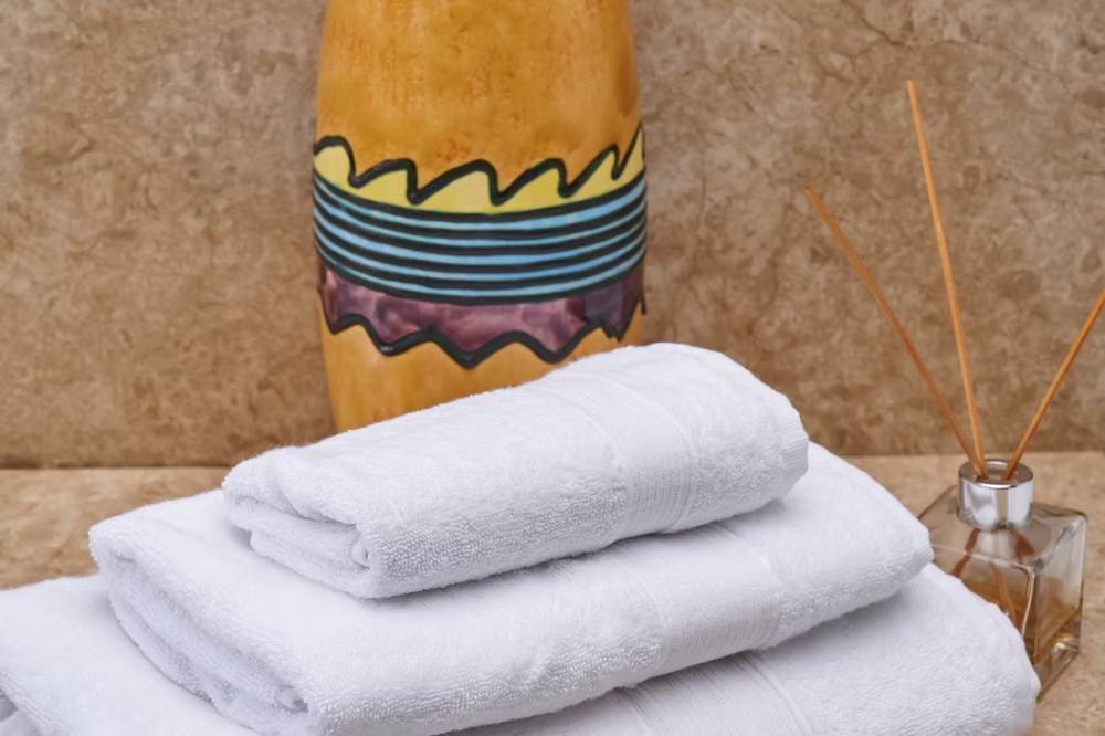 Sardegna Towel Set-Stack of white towels with a decorative vase and reed diffuser in the background.