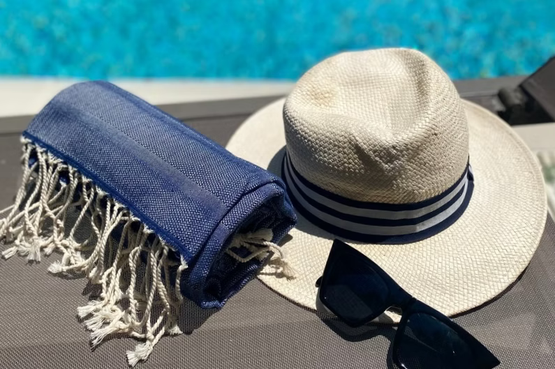 Sole Beach Towel (Navy)-Beige hat with blue stripes and sunglasses next to a blue towel by a pool