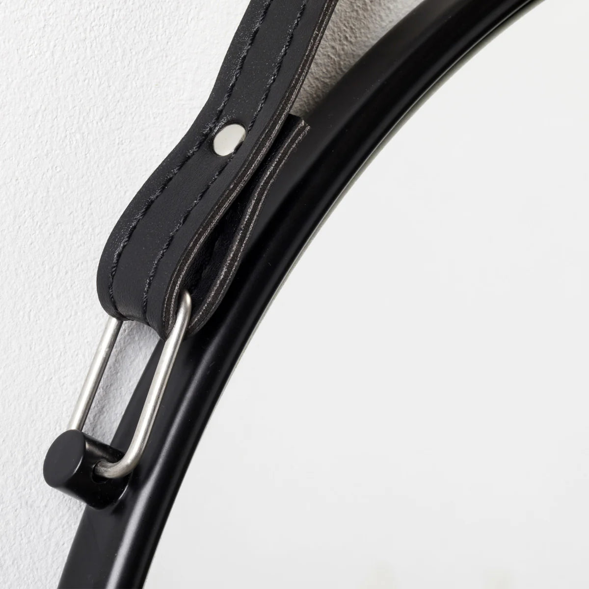 Close-up of a black leather belt with a metal buckle on a light gray background