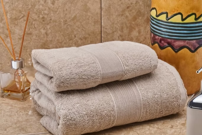 Verona Towel Set-Stack of beige towels on a bathroom counter with decorative items.