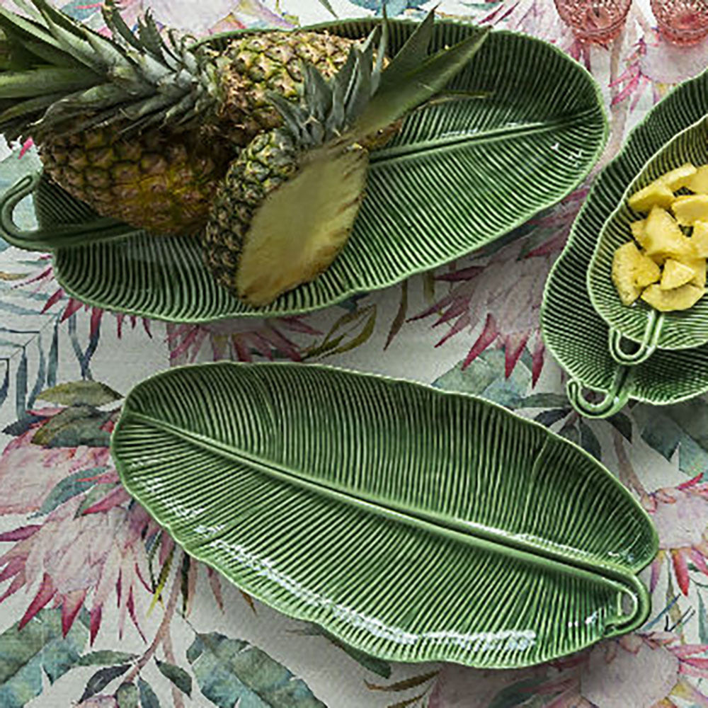 Green leaf-shaped ceramic plates with a pineapple on a floral tablecloth.
