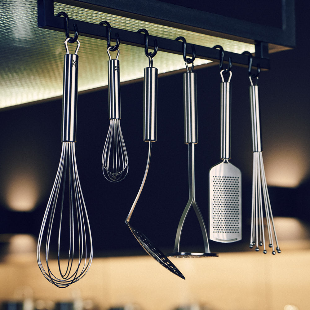 Set of kitchen utensils including whisks and a spatula hanging under a kitchen light.