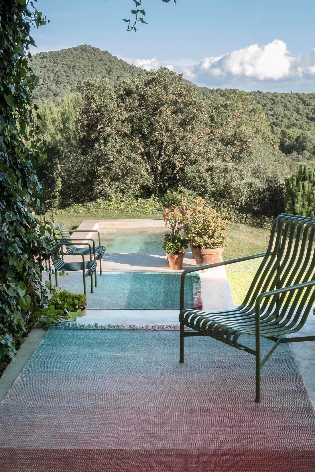 Nani Marquina brand-Outdoor setting with a pool, chairs, and potted plants surrounded by greenery.