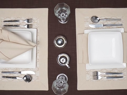 22 Maggio Istanbul Latte Placemat Set of 4-Elegant table setting with white plates, silverware, and glasses on a brown tablecloth.