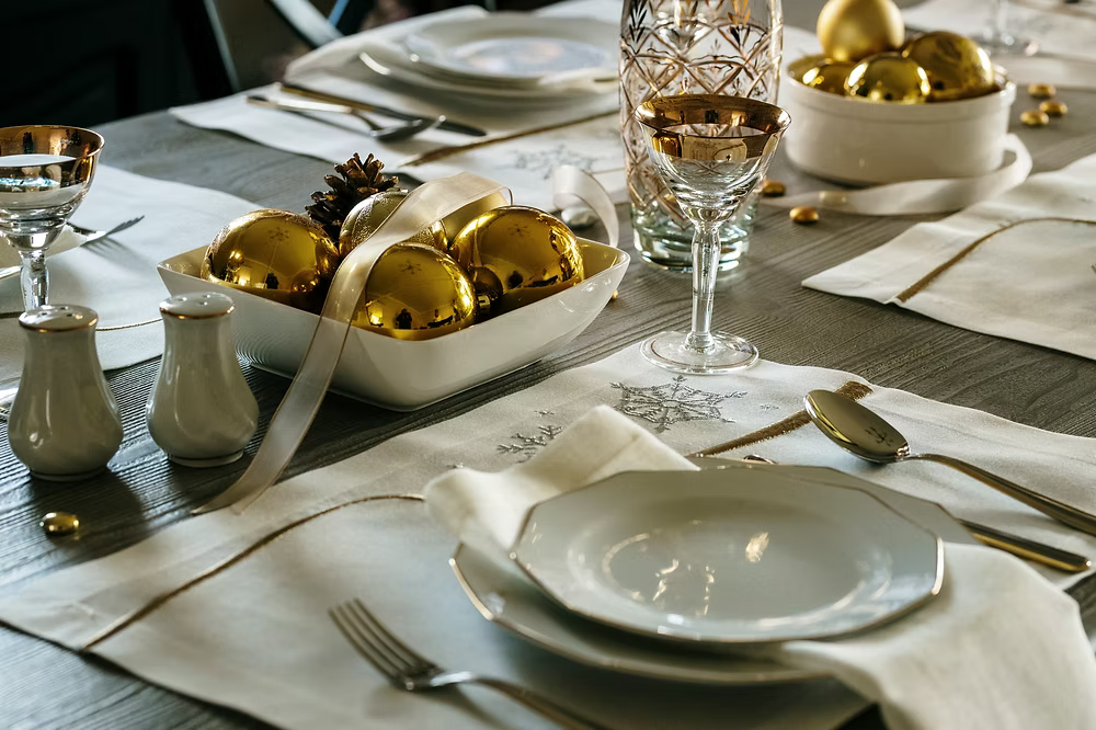 22 Maggio Istanbul Le Alpi  New Year Placemat Set of 4-Elegant table setting with gold ornaments and white plates on a wooden table.