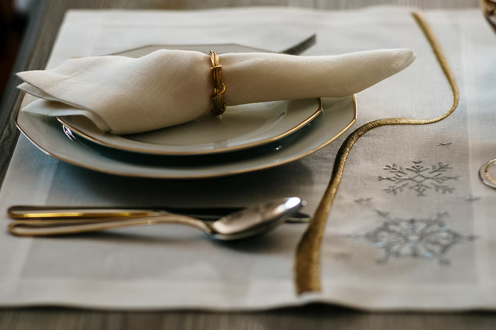 22 Maggio Istanbul Le Alpi  New Year Placemat Set of 4-Elegant table setting with folded napkin, plates, and cutlery on a decorative tablecloth.